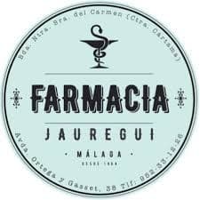 Circular logo with a light mint-green background and dark teal text and graphics, featuring a central caduceus symbol above the bold uppercase word 'FARMACIA', followed by 'JAUREGUI' in smaller uppercase letters; the outer ring contains the text 'Bda. Ntra. Sra. del Carmen (Ctra. Cártama)' at the top and 'Avda. Ortega y Gasset, 28 Tlf: 952 33 18 56' at the bottom, with small decorative flourishes flanking the central text block; the design conveys a classic, trustworthy pharmacy identity with clean typography and balanced layout.